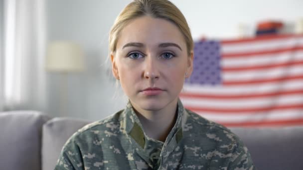 Mujer triste soldado en uniforme de camuflaje mirando a la cámara, fondo de la bandera de EE.UU. — Vídeos de Stock