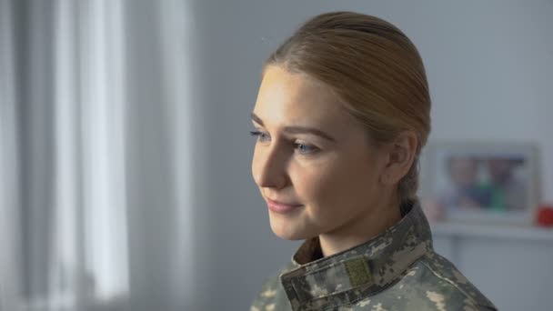 Feliz soldado mujer en uniforme de camuflaje viendo la marcha militar en la ventana — Vídeos de Stock