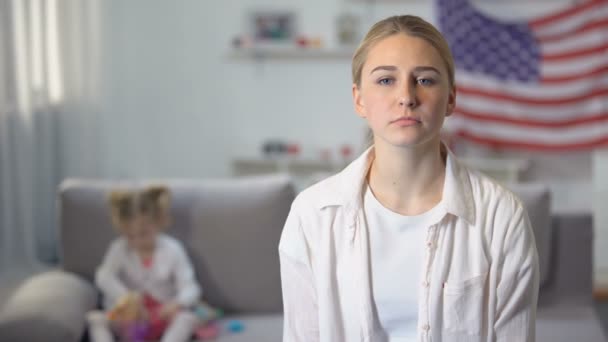 Traurige alleinerziehende Mutter blickt in die Kamera Tochter spielt auf Sofa gegen Flagge der USA — Stockvideo