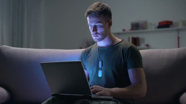 Чоловічий солдат, який друкує на ноутбуці, вдень і вночі психологічна онлайн-підтримка — стокове відео