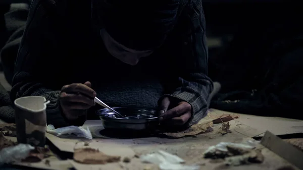 无家可归的人贪婪地吃汤从钢碗 肮脏的住所 — 图库照片