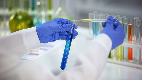 实验室助理在含蓝色化学物质的管内滴下黄色液体 — 图库照片