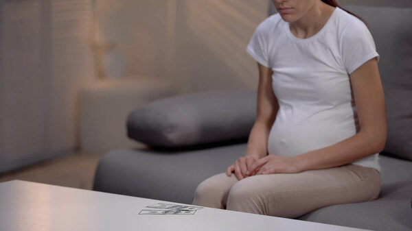 Разочарованная суррогатная мать смотрит на долларовые банкноты на столе, трудное решение
