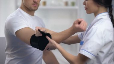 Gülümseyen doktor dirsek yastıklı ortez sabitleme sporcu hasta memnun, rehabilitasyon