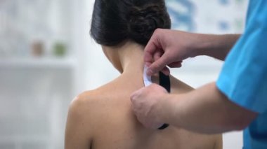 Kadın hastanın üst sırtına Y şeklinde bantlar uygulayan erkek hekim, sağlık