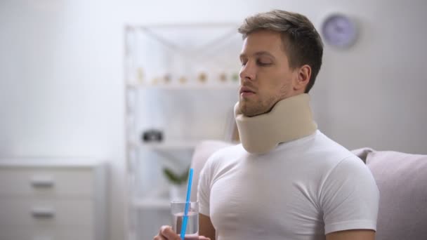 Man in foam cervical collar trying to drink glass water with straw, poor attempt — Stock Video