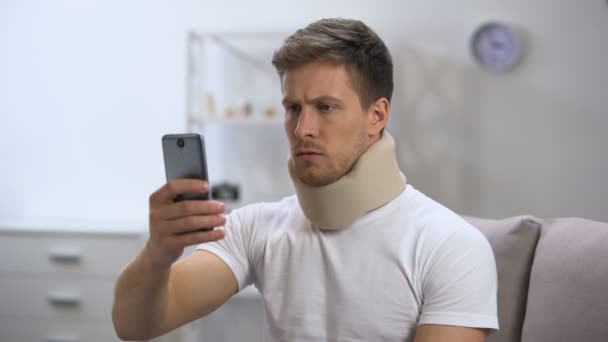 Человек в пеноворотнике читает сообщение по мобильному телефону, чувствует боль в шее — стоковое видео