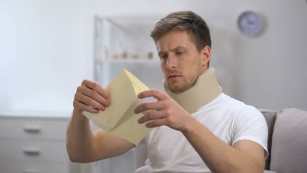 Man in foam cervical collar reading medical bill shocked with high price, health — Stock Video
