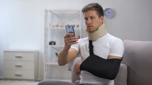 Mężczyzna w ramię procy i pianki szyjki macicy kołnierz przewijania na smartfonie, okres Rehab — Wideo stockowe
