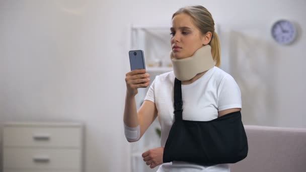 スマートフォン上の泡の子宮頸部襟と腕のスリング読書メッセージで悲しい女性 — ストック動画