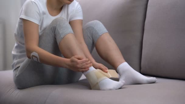 Female applying two-strap ankle wrap, suffering foot edema after sport trauma — Stock Video