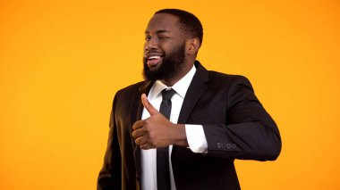 Takım elbiseli kendinden emin afro-amerikan işadamı başparmak-up ve göz kırpma yapma, reklam