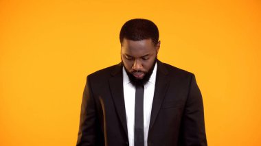 Formalgiyimli siyah adam suçlu hissederek aşağı bakıyor, sonuçlarını düşünüyor.
