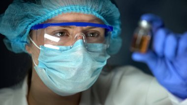 Scientist analyzing transparent brownish liquid in bottle, antidote development clipart