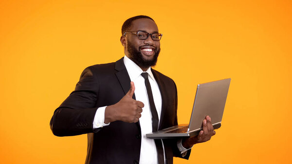 Inspired afro-american office employee holding laptop and showing thumbs-up