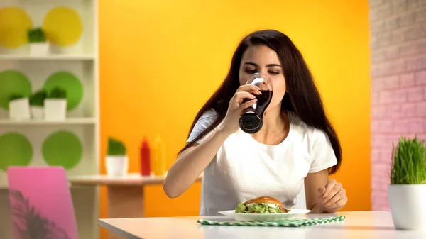 口渴的女人在快餐店喝甜饮料 在盘子里吃汉堡 — 图库照片
