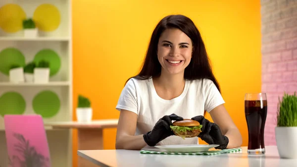 穿着黑色橡胶手套的快乐女人拿着汉堡包 对着镜头微笑 — 图库照片