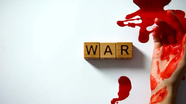 War word made of wooden cubes, bleeding hand on table, political conflict