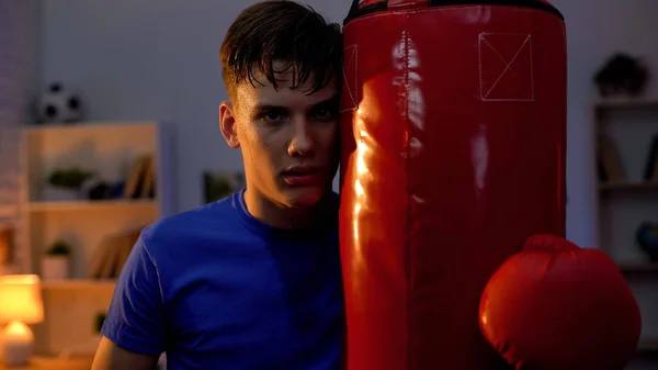 Exhausted teenager resting near boxing bag looking into camera, determination