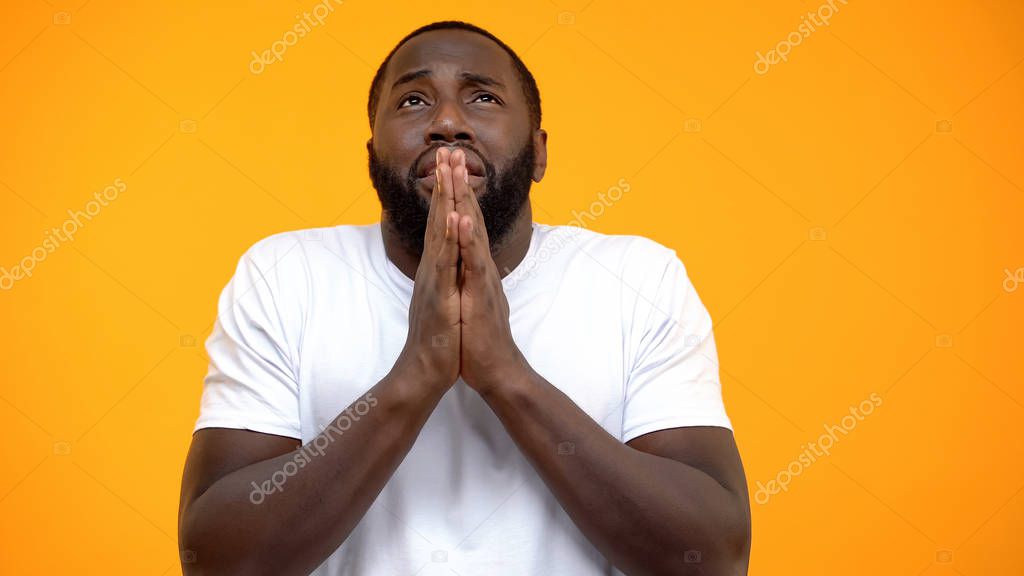 Afro-American man praying and looking up isolated on yellow background, belief