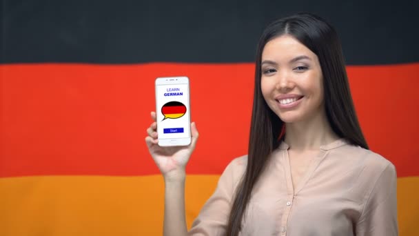 Mujer mostrando el teléfono celular con aprender alemán aplicación, bandera de fondo, educación — Vídeos de Stock