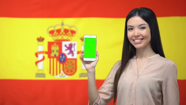 緑の画面で携帯電話を示す女性、背景にスペインの旗、旅行アプリ — ストック動画