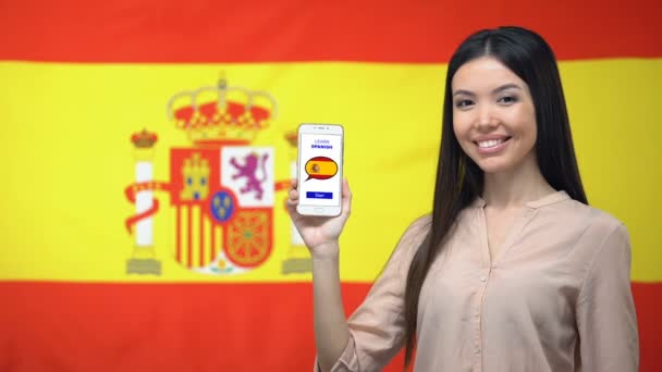 Mujer sosteniendo el teléfono celular con aprender español aplicación, bandera de fondo, educación — Vídeo de stock