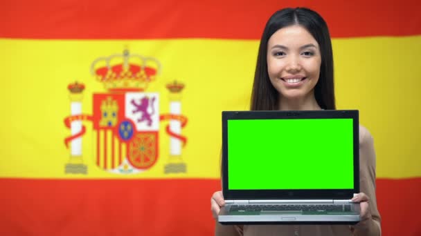 Estudiante sosteniendo portátil con pantalla verde, bandera de España en el fondo — Vídeos de Stock