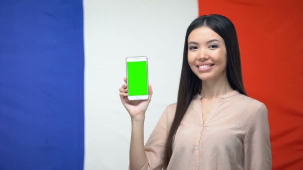 Señora mostrando teléfono inteligente con pantalla verde, bandera francesa en el fondo, aplicación de viaje — Vídeo de stock