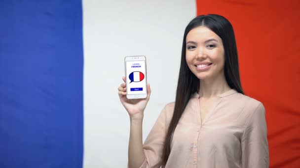 Menina segurando telefone com aprender aplicação francesa, bandeira em segundo plano, educação — Vídeo de Stock