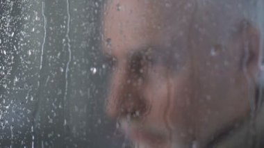 Üzgün yaşlı adam yağmurlu havalarda pencereden bakıyor, hayatı hakkında yakın çekim düşünüyor