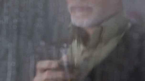 Meneer langzaam het drinken van whisky thuis, genieten van regenachtig weer buiten venster — Stockvideo