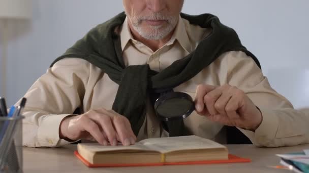 Senior man lezen boek door middel van Vergrootglas, visie aandoeningen op oudere leeftijd — Stockvideo