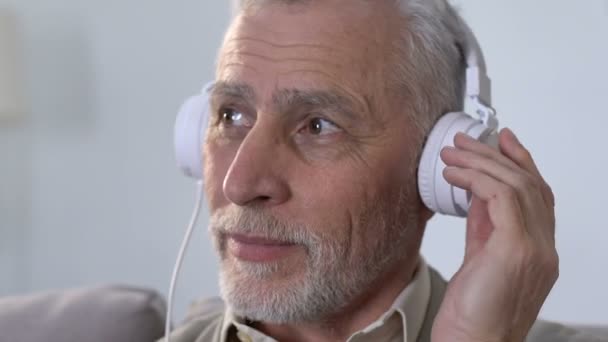 У віці чоловік у навушниках слухає музику, рухається в ритмі, сучасному стилі — стокове відео