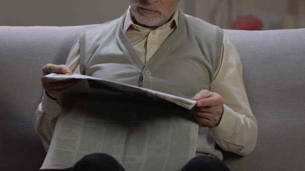 Senior man sitting on sofa at home, reading latest daily news in printing media — Stock Video