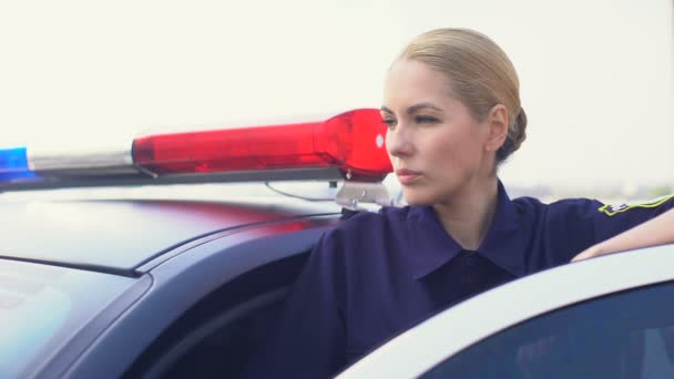 Mujer policía confiada mirando a la distancia de pie detrás de la puerta del coche de policía — Vídeos de Stock