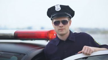 Güvenli polis memuru üniformalı ve güneş gözlüğü devriye arabası yakınında ayakta