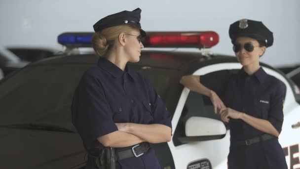 Polis üniformalı iki kadın devriye arabasının yanında durup gülümseyerek, kanun ve düzen — Stok video