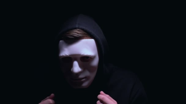 Mann mit schrecklicher Gesichtsmaske starrt vor dunklem Hintergrund in die Kamera, Terrorismus — Stockvideo