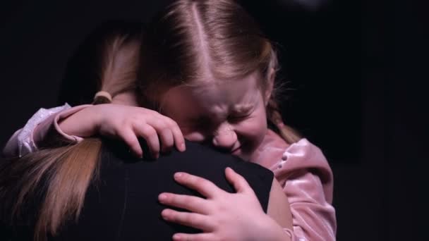 Beangstige meisje knuffelen moeder en huilen tegen zwarte achtergrond consternatie — Stockvideo