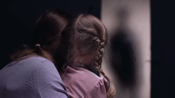 Scared woman hugging child, afraid of cruel criminal silhouette entering room — Stock Video