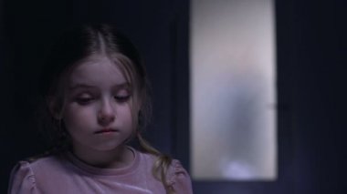 Ağlayan küçük kaçırılan kurban kameraya bakıyor, kapının dışında suç gölgesi