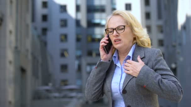 Gestora anciana sintiendo dolor repentino en el pecho hablando por teléfono, nerviosismo — Vídeos de Stock