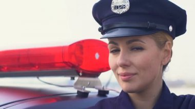 Bayan polis memuru şapkalı devriye arabasının yanında duruyor ve gülümsüyor, kanun koruma
