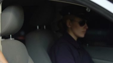 Polis kadın arabaya biniyor ve emniyet kemeri bağlıyor, kadın polis ekibi uzaklaşıyor