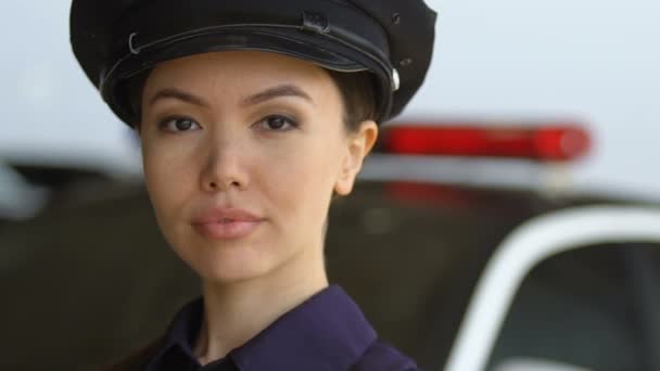 Asian policewoman in hat looking to camera and smiling, standing near squad car — Stock Video