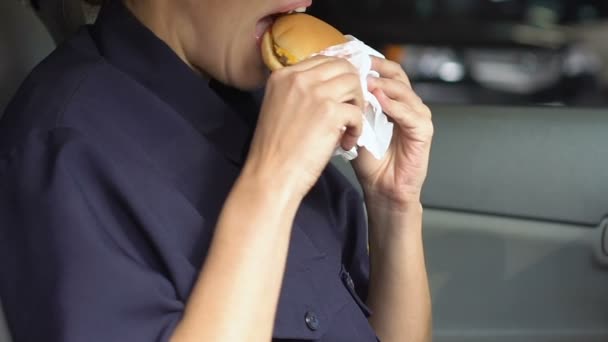 パトロール女性は車の中で脂肪ハンバーガーを噛む、空腹の警察官、不健康な食べ物 — ストック動画