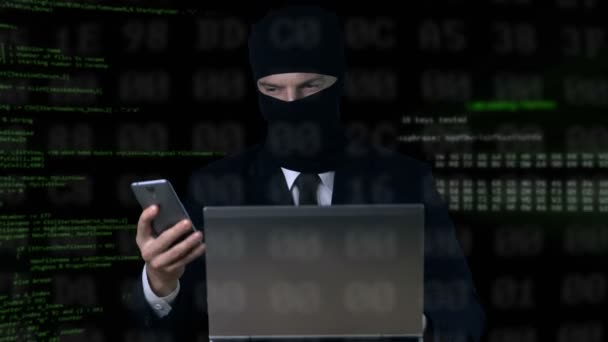 Criminal in suit and balaclava breaking security code using laptop and phone — Stock Video