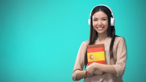 Chica escuchando lecciones de audio español en auriculares, libro en las manos, traducciones — Vídeo de stock