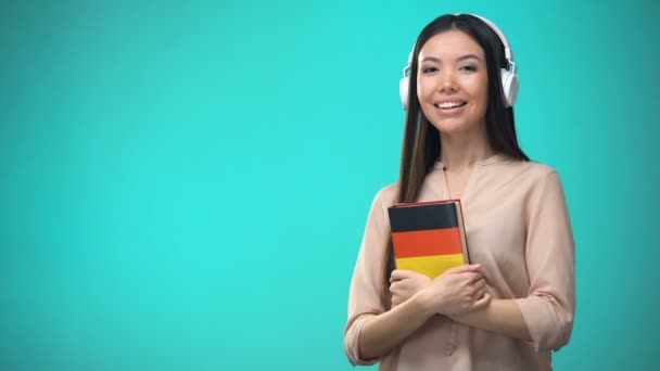 Menina ouvir aulas de áudio alemão no fone de ouvido, livro em mãos, traduções — Vídeo de Stock